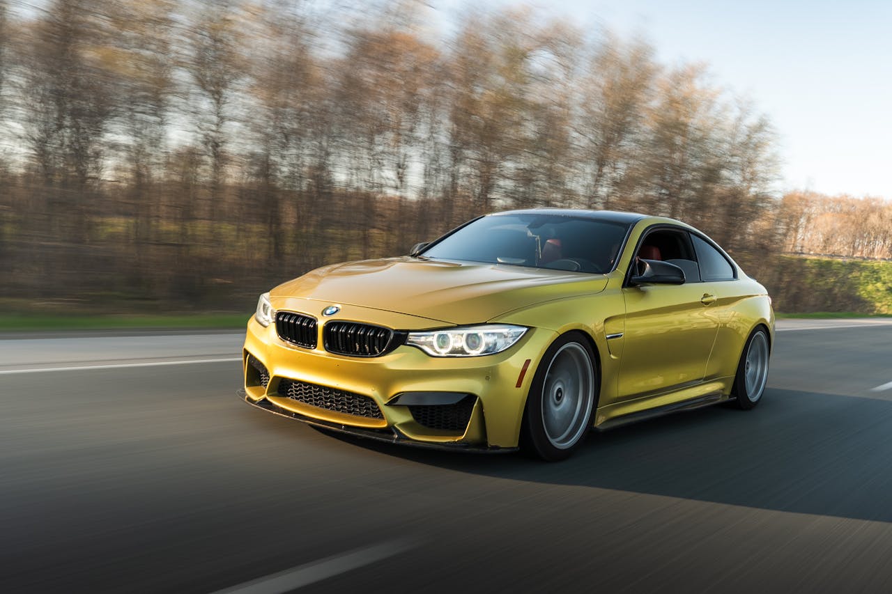 A sleek gold sports car speeds along an open road amidst a natural backdrop, showcasing dynamic motion.