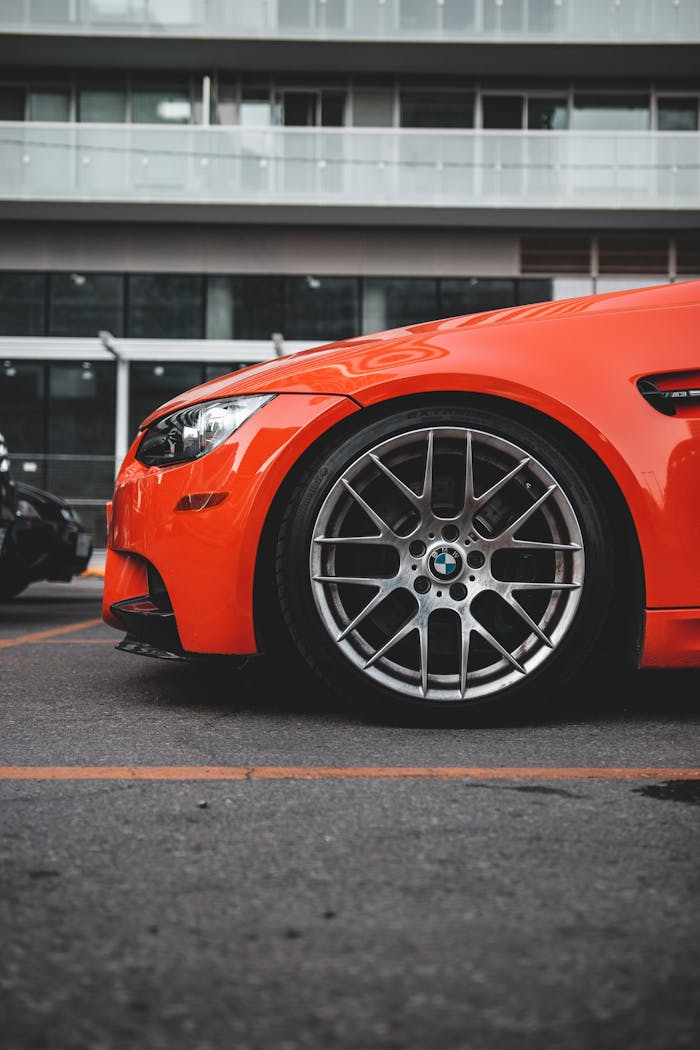 About Close-up of an orange BMW car parked in a city parking lot, showcasing its sleek design and wheels.